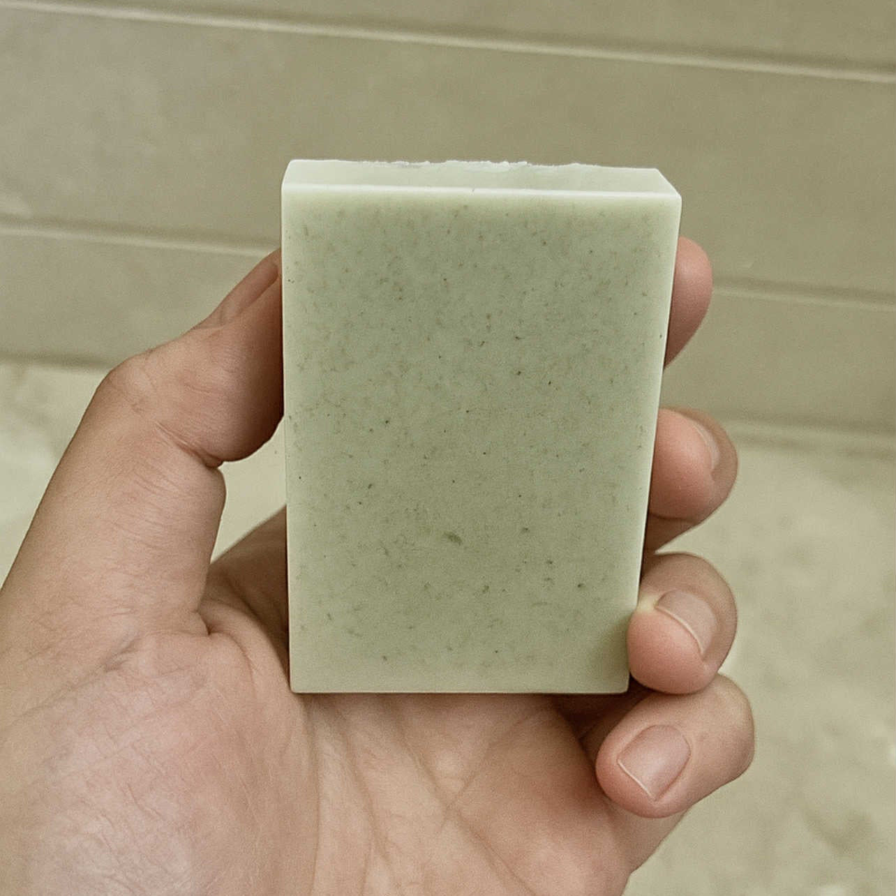 Hand holding a rectangular bar of soap against a neutral background
